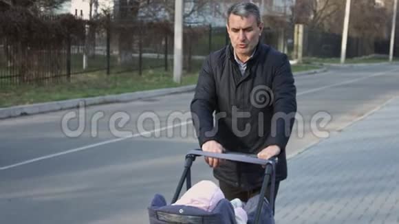 成熟男人推婴儿车在美丽的春天散步祖父和孙女慢动作视频的预览图