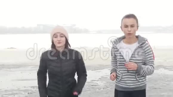 两个穿着秋装的运动女子在雪地海滩上奔跑视频的预览图