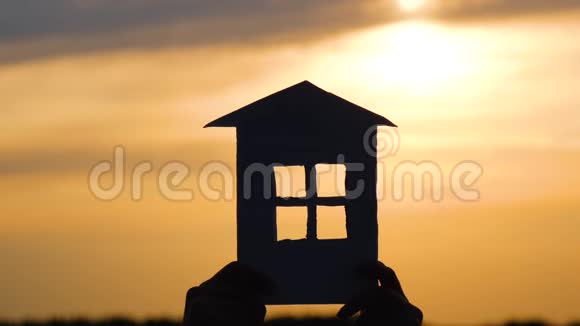 夕阳背景下模型纸建筑的剪影手拿着房子的概念视频的预览图