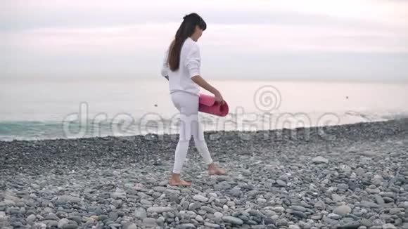 女人躺在鹅卵石滩上做运动瑜伽垫白天练习视频的预览图