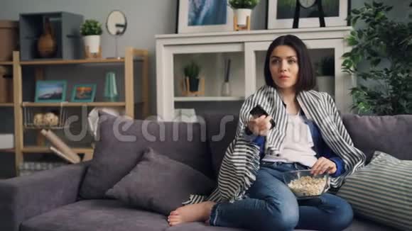 看电视的年轻女士笑着吃爆米花独自在家玩视频的预览图