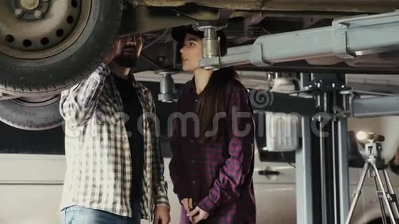 一个漂亮的女孩一个汽车修理工正在学习如何修理一辆汽车一个更有经验的人一个汽车悬架视频的预览图