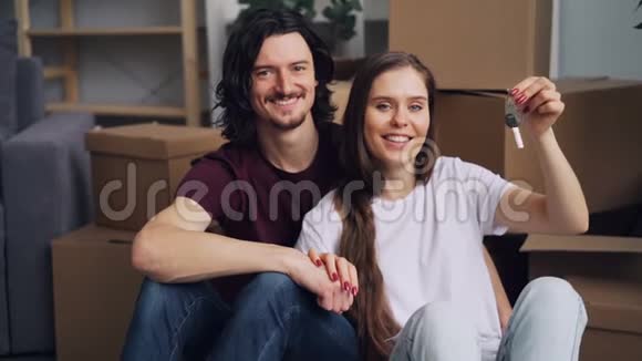 慢镜头肖像幸福夫妇拿着钥匙坐在新公寓的地板上视频的预览图