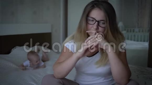 心理健康焦虑不安的戴着眼镜的女人坐在床上在爬着婴儿视频的预览图