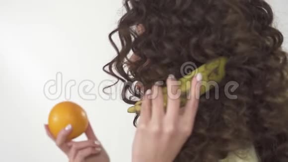 描绘了一个年轻的卷发女孩她长着鲜艳的妆容饶有兴致地看着橙色模仿电话交谈视频的预览图