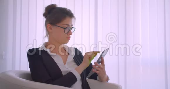 年轻漂亮的白种人女商人用平板电脑拍摄特写镜头用绿色屏幕拍摄坐在里面的镜头视频的预览图