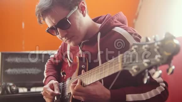 一个戴着耳机和眼镜的音乐家在录音室里弹吉他录制旋律视频的预览图