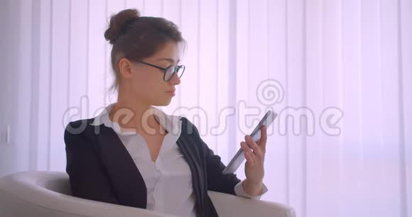 年轻漂亮的白种人女商人用平板电脑拍摄特写镜头用绿色的彩色屏幕拍摄坐着的照片视频的预览图