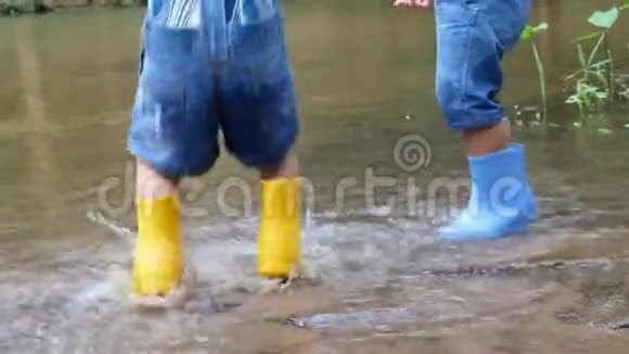 穿着靴子的亚洲小孩玩着在河岸的水坑里跳视频的预览图