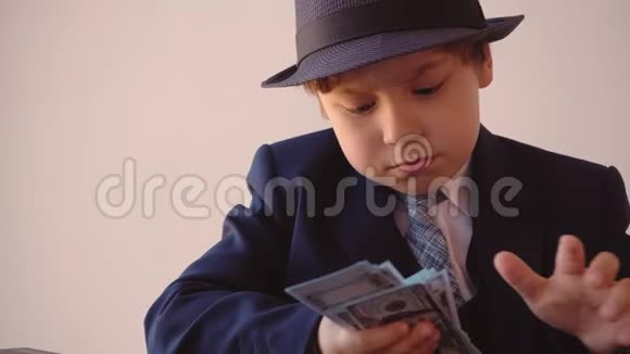 小男孩看起来像一个戴帽子和西装的商人用放大镜看美元视频的预览图