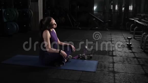 年轻漂亮的女孩在健身房锻炼前揉捏她的头和脖子坐在地板上积极地做循环移动视频的预览图