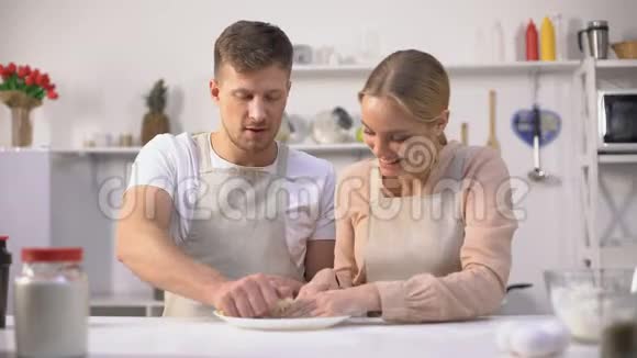 快乐的一对夫妇笨拙地揉着面团在厨房里一起度过快乐的时光视频的预览图