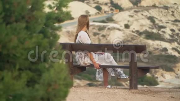 年轻漂亮的女人一头漂亮的金发坐在高高的山上的长凳上视频的预览图