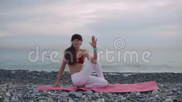 运动的女人正在伸展身体白天坐在鹅卵石海岸上视频的预览图