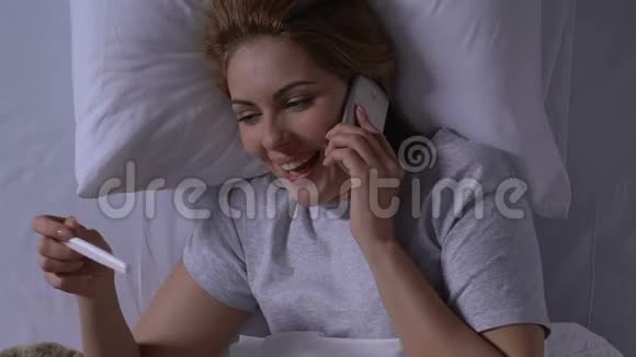 在床上微笑的女人拿着怀孕测试和通话电话结果阳性视频的预览图