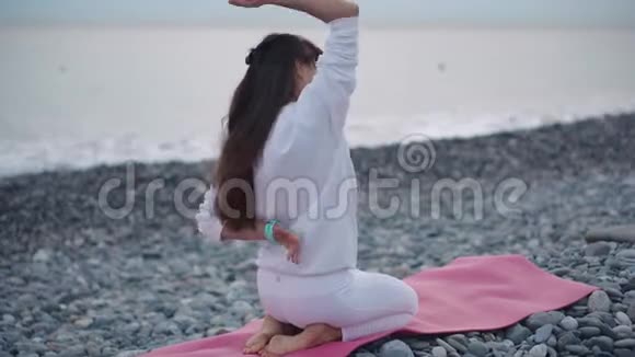 女运动员背着手坐在鹅卵石滩上望着大海视频的预览图