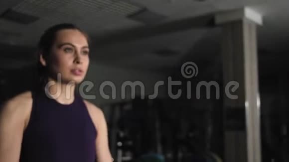 年轻漂亮的女孩在健身房锻炼用金属哑铃向前举起双手镜头对准哑铃视频的预览图