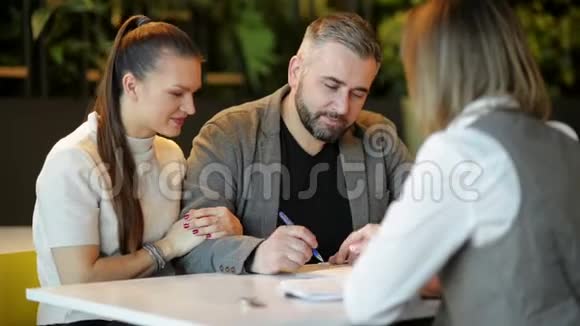 房地产经纪人和年轻夫妇坐在办公桌旁讨论出售房产幸福的夫妻成了一所房子视频的预览图