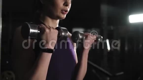 年轻漂亮的女孩在健身房训练举起金属哑铃手快关门镜头聚焦哑铃视频的预览图