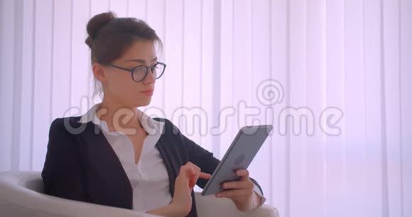 一位年轻漂亮的白种人女商人坐在扶手椅上看着镜头正在制作平板电脑视频的预览图