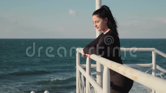 美丽的黑发女子站在码头上晨练后在海上欣赏令人敬畏的景色视频的预览图
