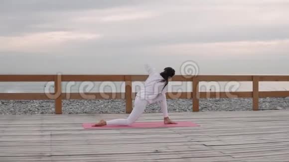 女运动员正在更换瑜伽体式坐在地板上在海景背景下视频的预览图