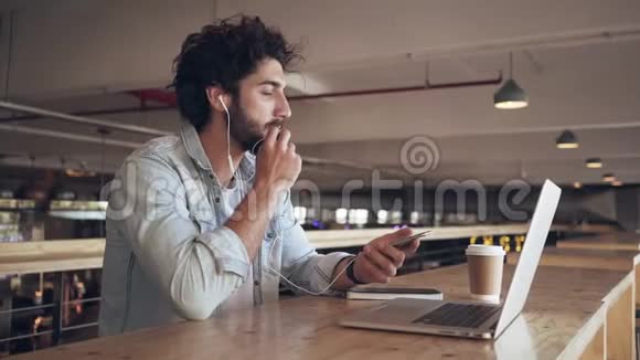 一个人在咖啡馆里通过耳机用智能手机说话视频的预览图