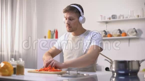 积极的男人听音乐和烹饪蔬菜健康的低热量饮食视频的预览图