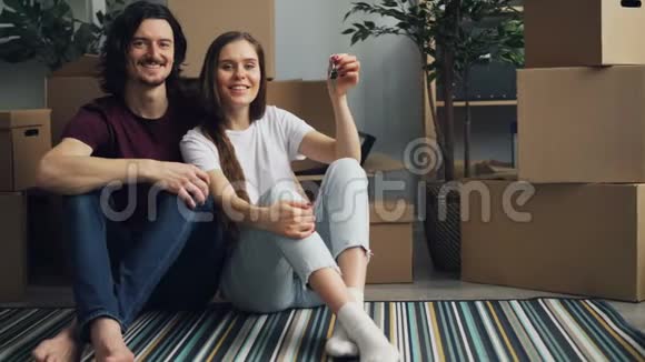 一对夫妇拿着钥匙坐在地板上的新公寓周围有盒子视频的预览图