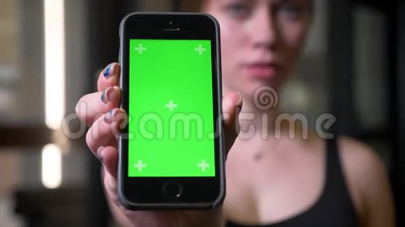 健身房里模糊女运动员拿着带有彩色绿色屏幕的手机的特写镜头视频的预览图