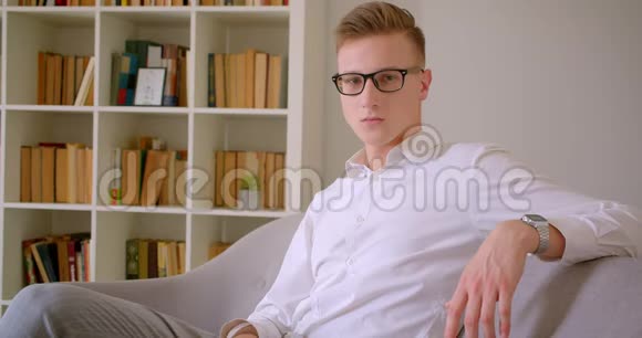 年轻英俊的白种人商人戴着眼镜坐在沙发上看着室内摄像机的特写照片视频的预览图