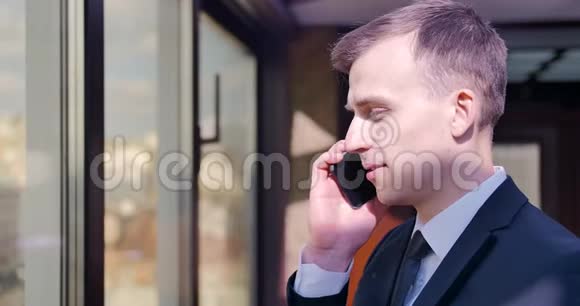 一个穿西装的年轻人站在办公室的窗户附近打电话挂断电话高兴起来满意视频的预览图