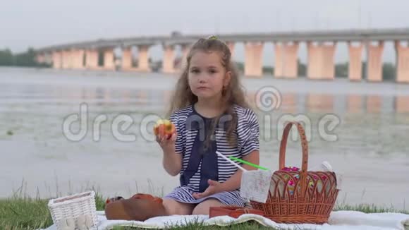孩子们休息小可爱的女孩在河边的大自然野餐时吃新鲜的苹果视频的预览图