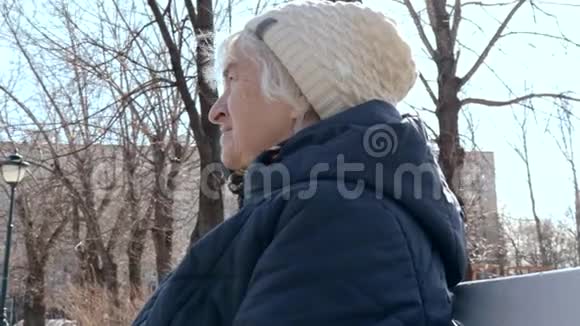 一位孤独抑郁的老年妇女在阳光明媚的早春坐在城市公园的长凳上的肖像视频的预览图