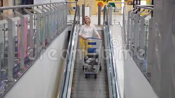 一个女人拿着一辆手推车从超市的自动扶梯上下来视频的预览图