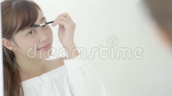 美丽的年轻亚洲女人涂妆眉刷美丽的亚洲女孩用化妆品做化妆风格的镜子视频的预览图