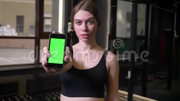 运动女孩显示智能手机与彩色绿色屏幕进入相机是严重的集中在健身房视频的预览图