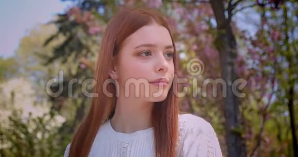 穿着白色衬衫的迷人的生姜女孩在粉红色的花圃里摆成相机变换的姿势视频的预览图