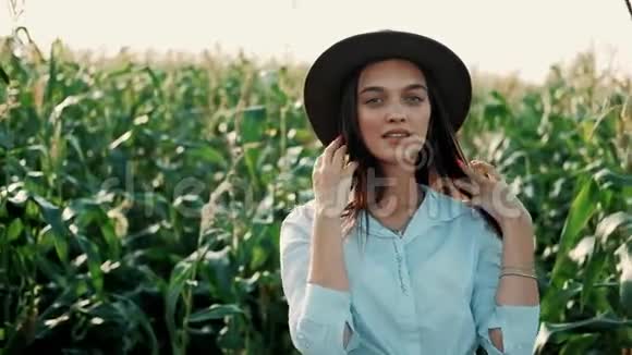 戴着帽子的美丽少女站在玉米地边微笑在夕阳下看镜头的画像视频的预览图