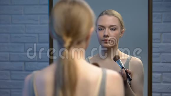 漂亮的年轻女性在镜子前涂粉在镜头前微笑视频的预览图