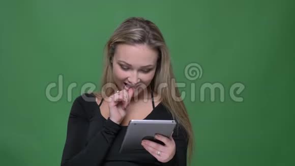 女商人穿着黑色衬衫看着平板电脑聚精会神地转向相机在绿色的背景下微笑视频的预览图