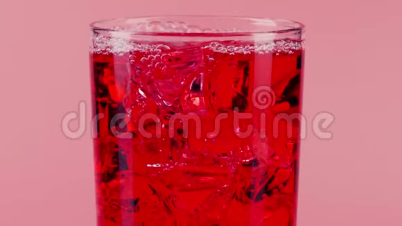 红色软饮料粉红色背景下的玻璃杯中有冰块红色特写慢镜头视频的预览图