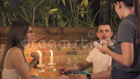 男人和女人在晚上的餐厅里用蜡烛订购浪漫晚餐的食物从快乐中得到命令的服务员视频的预览图