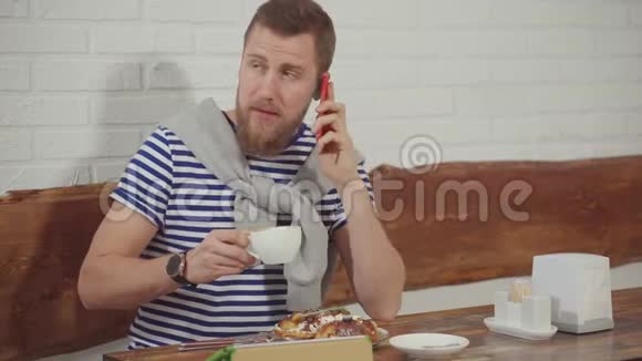 男人坐在咖啡馆里喝着咖啡一边打电话聊天一边开心地笑着视频的预览图