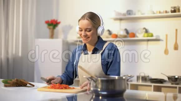 积极的女孩听音乐和烹饪蔬菜健康的低热量饮食视频的预览图