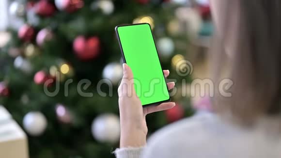 在圣诞装饰附近使用绿色锁屏智能手机的妇女视频的预览图