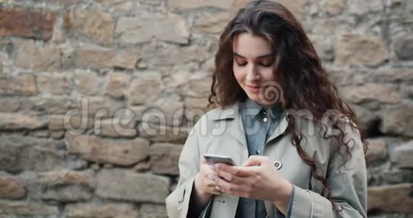 漂亮女孩用智能手机在街道触摸屏幕上缓慢移动微笑视频的预览图