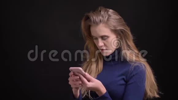 年轻的金发模特用智能手机刷触摸屏集中在黑色背景上视频的预览图