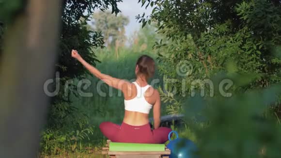 健康的健身女性莲座式身体倾斜坐在绿色的木桥上视频的预览图
