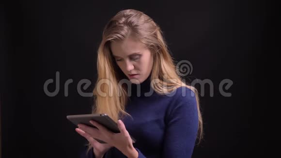 年轻的金发模特用平板电脑刷触摸屏注意黑色背景视频的预览图